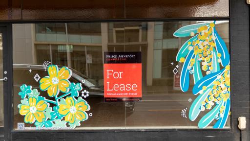 A shop window with a for lease sign and flower art on the window
