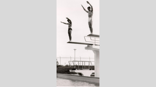 Two people standing at the top of diving boards, ready to dive into the pool.