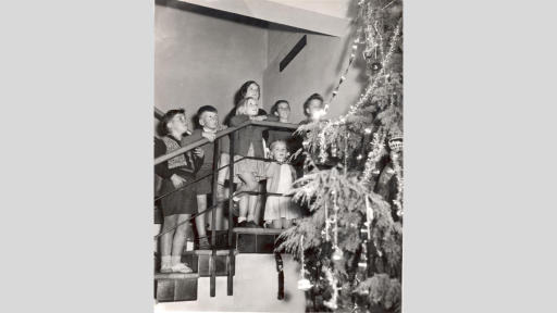 Children standing on stairs looking up at a tall Christmas tree.