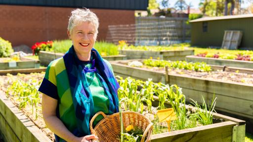 Woman standing in from of a veggie patch with a basket of veggies