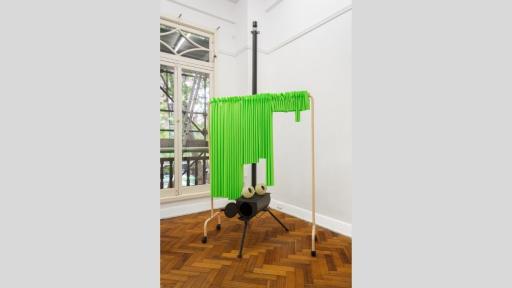 A smoker with lightbulbs placed on top to look like eyes. Above the smoker is a clothes horse with fluro green material hung on it like a curtain, and cleanly cut at various lengths.
