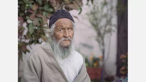 an older Indian man with a grey beard looking at the camera