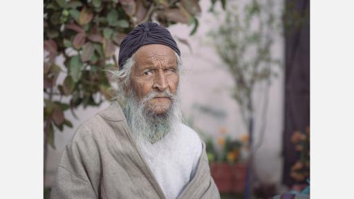 an older Indian man with a grey beard looking at the camera 