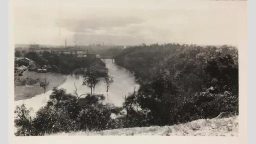 Photo looking down on a river and landscape from a hill industrial buildings on the skyline
