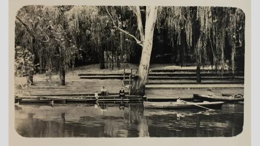 Photo of a docking area on a river with a person rowing a boat and people sitting by the river