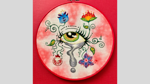 A circle of material with embroidery of an eye that has a tear coming out of it as well as vines with flowers.