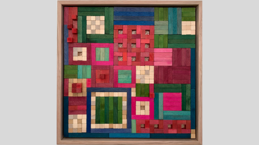 A framed piece of art made of wooden rectanges arranged in square patterns, some qith no piece in the middle of the square and some with raised pieces that emerge from the artwork. The pieces range from pink to greens and blue, as well as light browns.
