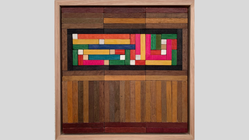 A framed piece of art made of wooden rectanges arranged to make a rainbow rectangle of blocks, surrounded by mainly horizontal blocks in dark brown shades
