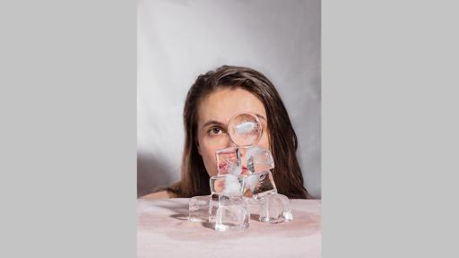 Photo by Hannah Phemister of a person with long hair looking at the camera from behind a small tower of large ice blocks