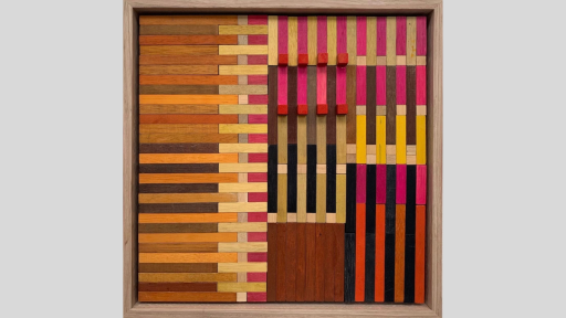 A framed piece of art made out of wooden rectangualr blocks that have been arranged in lines both horizonal and verticl to tesselate together and there are pink, yellow, and dark to light brown blocks used throughout the piece