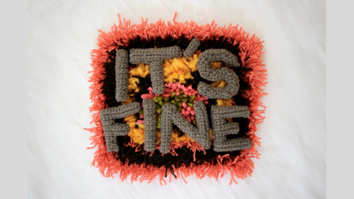 A piece of carpet with pink, black, orange, and green wool in concentric circles, overlaid with crocheted letters spelling out 'It's fine'
