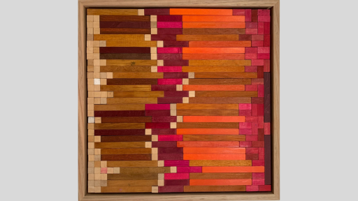 Aframed art piece made up of wooden blocks arranged horizonally in lines and progrssing in colour from light to dark brown, then to pink and orange and returning to pink