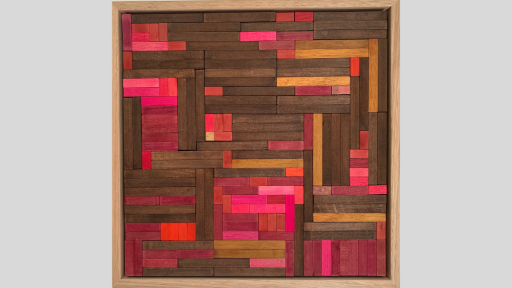 A framed piece of art made of wooden rectangles arranged in a herringbone pattern with pinks and dark browns throughout
