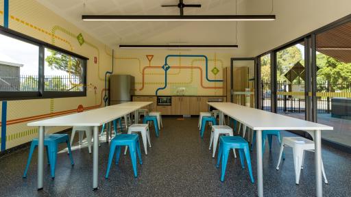 Inside the Kew Traffic School Party room with two long tables in the space, coloured road decals on the walls, and a kitchen with a fridge, oven and microwave.