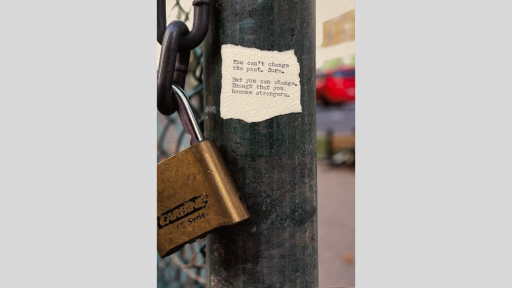 A piece of torn paper with a poem printed from a typewriter, stuck to a pole outside that is part of a chainlink fence and is next to a padlock