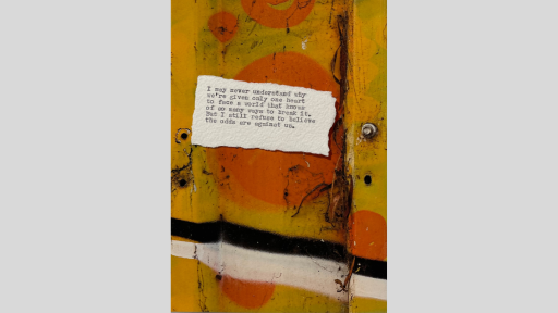 A piece of torn paper with a poem printed from a typewriter, sitting on an orange and yellow grafitti painted surface with a black and a white line painted across the surface under the paper