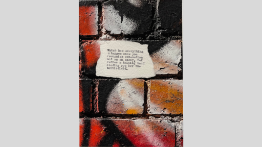 A piece of torn paper with a poem printed from a typewriter, sitting on a brick surface that has been grafittied with black, red, white and orange spray paint