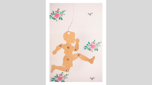 A 2 dimensional paper puppet of a small child in a running pose, in front of a background with pink flowers