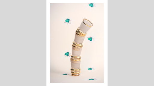 A stack of glasses with gold rims and frosting that is precariously leaning to one side, in front of a background of blue flowers