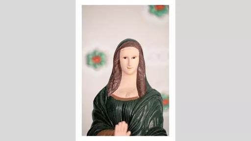 A religious looking figurine of a person in a green robe with their hand outstretched in a stopping motion