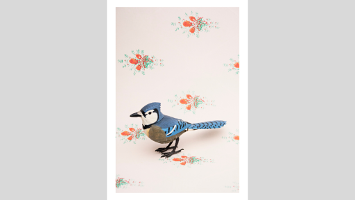 A figurine of a blue bird on a wallpaper background of green and red fleur de lises