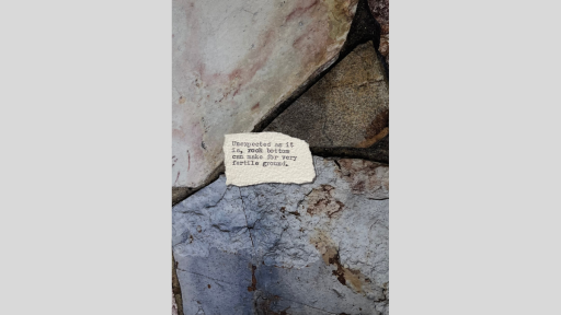 A piece of torn paper with a poem printed from a typewriter, sitting across some large rock tiles
