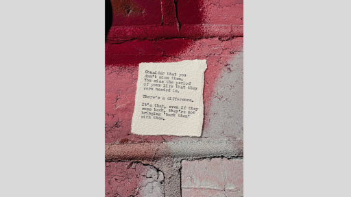 A piece of torn paper with a poem printed from a typewriter, sitting on a textured surface that is pink ad white and looks like large brickwork
