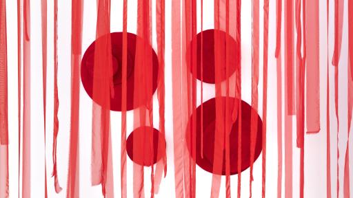 Strips of red hanging material in front of a wall with large red circles mounted on it.