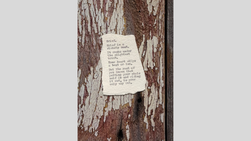 A piece of torn paper with a poem printed from a typewriter, sitting on a wooden textured surface that has flakign whit epaint revealing natural wood colouring