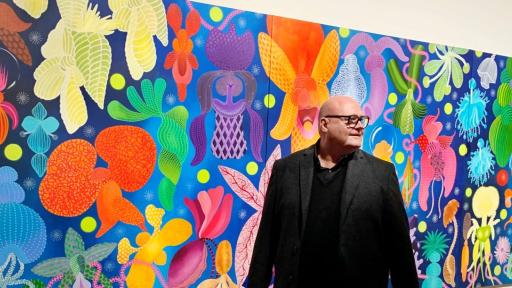 Michael McHugh in front of his artwork featuring a variety of flowers in bright colours across a large blue canvas