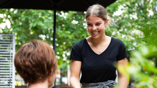 A staff member at an outdoor area of a cafe serving a customer with a smile