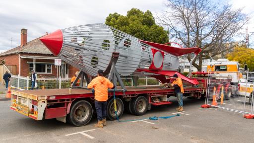 A large metal rocket being tied to the back of a truck