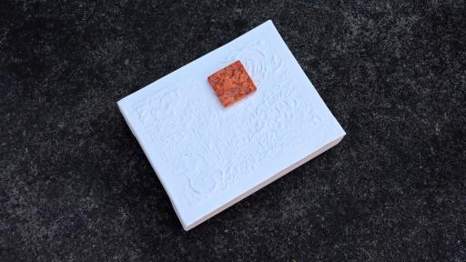 A ceramic artwork of a small orange square on a white background