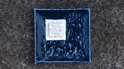 A ceramic artwork of an inky blue square with a pale duo of inlaid squares