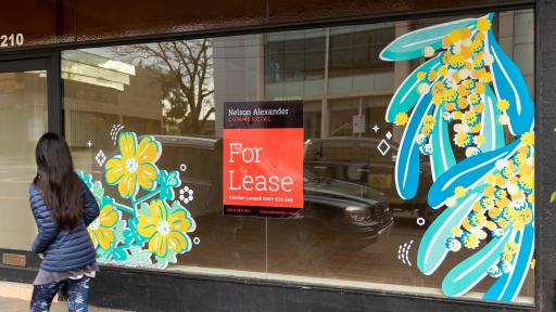 An empty shopfront window with two yellow and green painted floral designs on it