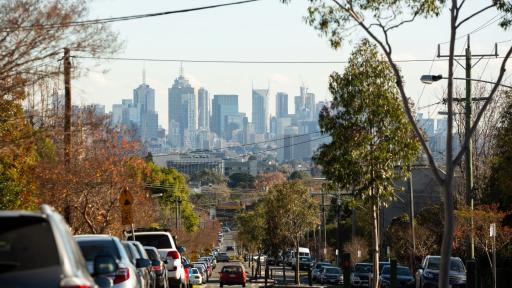Looking down a suburban street toward the city skyline, with cars parked along the street