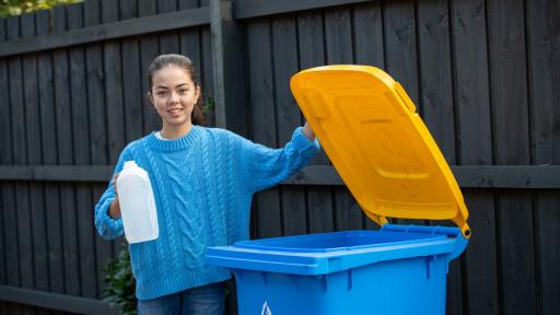 A young person holding an empty milk carton next to an open recycling bin