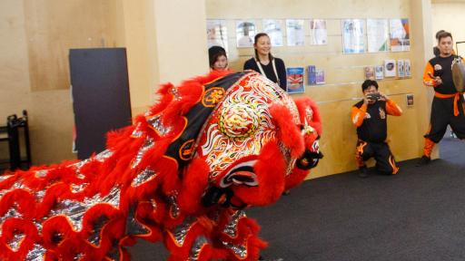 A traditional red and intricately designed chinese dragon costume dancing in front of a crowd in an indoor area