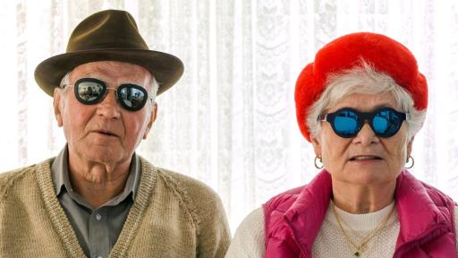 Two older people in front of a bright white background wearing modern reflective sunglasses