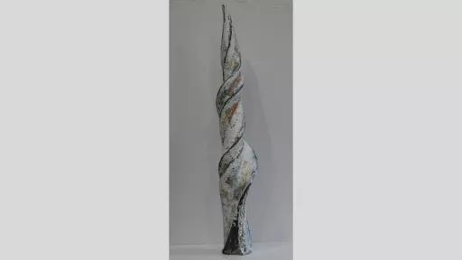 Vertical sculpture of a thick, twisted shape like a unicorn horn in white, gold and blue