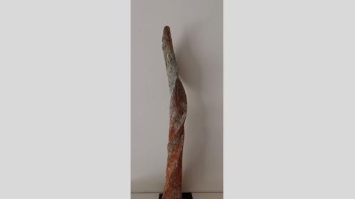 Vertical sculpture of a twisted shape like a unicorn horn in rusty orange and white