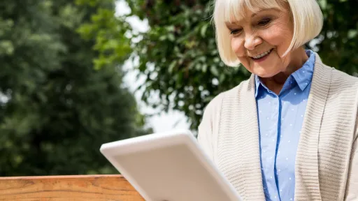A woman over 55 smiles down at her iPad outdoors