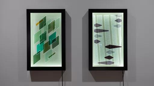 Two vertical-rectangular artworks on a wall. One features scattered grey and black diamond shapes and one features green overlapping diamond shapes.