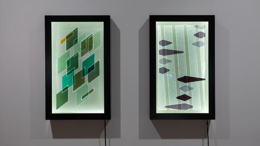 Two vertical-rectangular artworks on a wall. One features scattered grey and black diamond shapes and one features green overlapping diamond shapes.