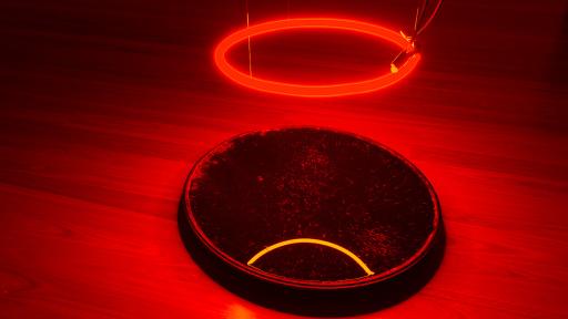 Art installation featuring a red illuminated circle hanging over a black reflective circle on the ground.