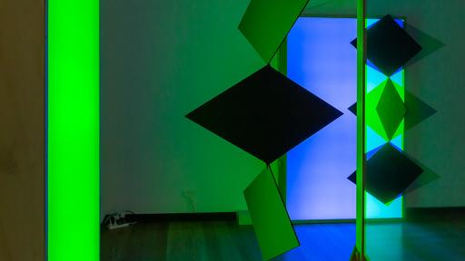 Art installation featuring three diamond shapes hanging from a fitting, and three diamond shapes on a glowing purple background.