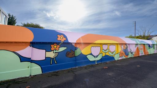 a colourful mural on a railway bridge, of a hand holding out flowers beneath a rainbow