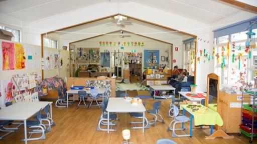 A light-filled, colourful kindergarten room with tables, chairs, bunting and artworks