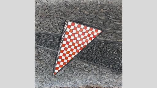 An artwork featuring a red and white checkered pyramid emerging from a surface made of closely layered stones