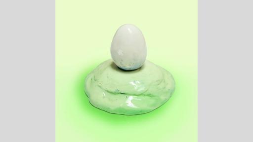 Ceramic sculpture of a white egg on a light green mound. 